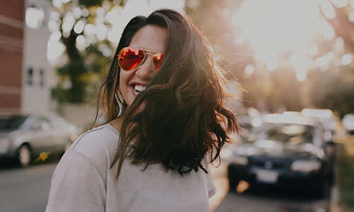 smiling woman with sunglasses walks through city